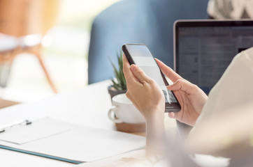 female hand using smartphone while working at desk in office