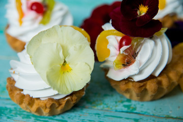 dessert: a set of cakes with cream and edible flowers (Pansy) on a blue wooden background. the concept of vegetarianism and healthy eating