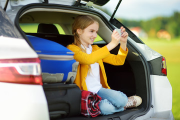 Wall Mural - Adorable little girl ready to go on vacations with her parents. Kid playing with her phone in a car.