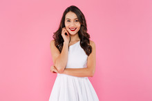 Portrait Of Asian Lovely Woman With Dark Curly Hair In White Dress Posing With Kind Smile, Isolated Over Pink Background