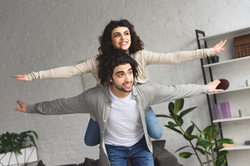 Wall Mural - boyfriend giving piggyback to laughing girlfriend and they pretending flying at home