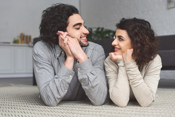 Canvas Print - smiling young couple lying on floor and looking at each other at home