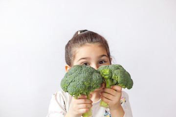 Happy little girl eating fresh vegetables. A portrait of cute child girl on a white background. Healthy teeth.