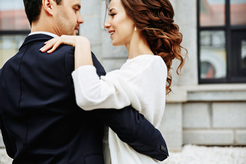 the groom holds his bride in his arms and they dance near the building with beautiful windows