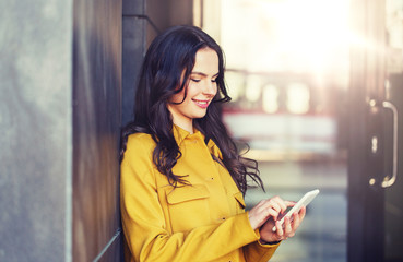 Wall Mural - technology, communication and people concept - smiling young woman or girl texting on smartphone on city street