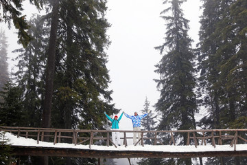 Canvas Print - Happy couple standing on bridge in snowy forest. Winter vacation