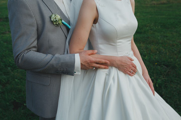 Wall Mural - Elegant wedding couple is hugging outdoors. Groom in checkered grey suit and tiffany light blue bow tie. Bride in satin white dress. Summer romance. wedding buttonhole and white golden rings.