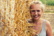 © AnastazjaSoroka - A smiling young woman with blond hair stands on the background of haymaking.