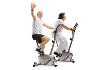 Canvas Print - Elderly man and an elderly woman riding exercise bikes with the man waving