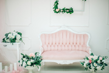 White studio with vases, blossomed, table and a vintage couch in pink. A styling, a luxurious interior