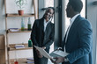 © LIGHTFIELD STUDIOS - smiling african american businessman with laptop and colleague near by in cafe