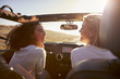 © Monkey Business - Two girlfriends driving with sunroof open look at each other