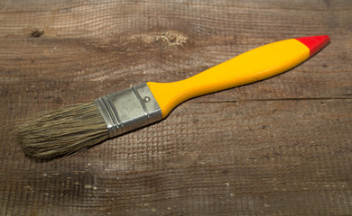 Paint brush width 1 inch with yellow handle on a wooden background close-up