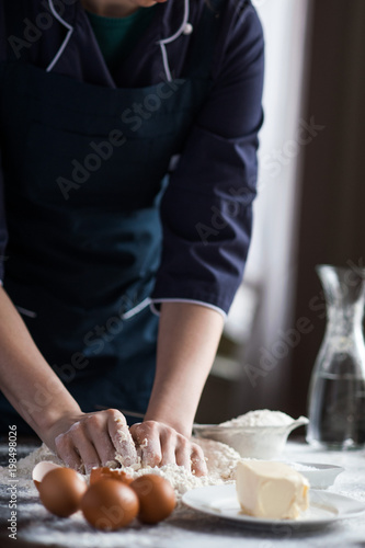 Plakat Image of hard working male cook or baker with dark skin wears apron, sheets well made dough, going to bake tart, isolated over black chalk background. Unrecognizable African American chef on kitchen