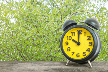 Wall Mural - Closeup yellow alarm clock show the time in 10 o'clock on wood desk and green leaves in the park textured background