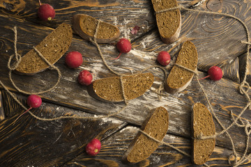 Wall Mural - Conceptual still life photography of pieces of bread tied with twine, lying on ancient wooden table made of rough boards among several red radishes