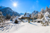 Fototapeta  - Small wooden house in winter landscape near Morskie Oko lake with sun on blue sky, Tatra Mountains, Poland