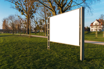 White clipped billboard in a park with the beautiful evening light - blank mockup -commercial and advertising concept