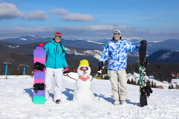 Sticker - Happy couple with snowman and snowboards at ski resort. Winter vacation