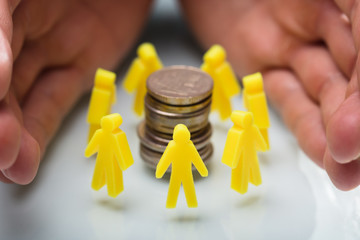 Wall Mural - Businessperson Protecting Stacked Coins And Yellow Human Figures