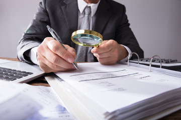 Businessperson Looking At Receipts Through Magnifying Glass