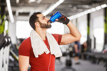 Bearded Muscular Man Wears Red T-shirt Drink Water From Blue Bottle In The Gym