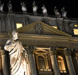 Heiligenstatue auf dem Petersplatz mit nächtlich beleuchteter Fassade des Petersdoms im Hintergrund