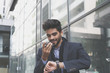 © Mladen - Smiling businessman in city checking time and talking on mobile phone.