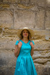 © Елена Кравчук - Smiling traveling girl near ancient wall, old stone background, blue dress, hat