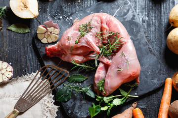 Whole Forest wild rabbit, Recipe with apple pie, Raw meat with spices and vegetables, Sea salt, red, white pepper and coriander in clay pots on an old black rustic table. copy space