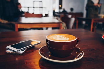 A cup of coffee on wooden surface with mobiles in cafe