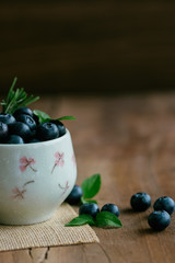 Wall Mural - Fresh ripe wild blueberries heap in white bowl on wood table in vertical with copy space for background. Healthy and delicious fruits concept. Blueberry is a high antioxidant food and vitamin C.