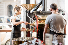 Man And Woman In Uniform Working With Roaster Machine Roasting Coffee Beans At The Cafe