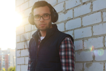 Portrait of a handsome young man with headphones. A man with a beard listens to his favorite music in large professional headphones on the street.