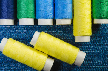 Wall Mural - Spools of yellow, blue and green threads on a denim fabric