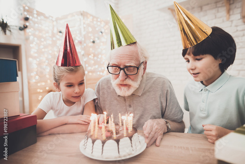 Download Grandfather Grandson And Granddaughter At Home Grandpa Is Blowing Candles On Birthday Cake Stock Photo Adobe Stock