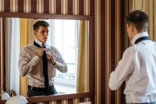 A Young Handsome Man Ties Up A Tie In Front Of A Mirror