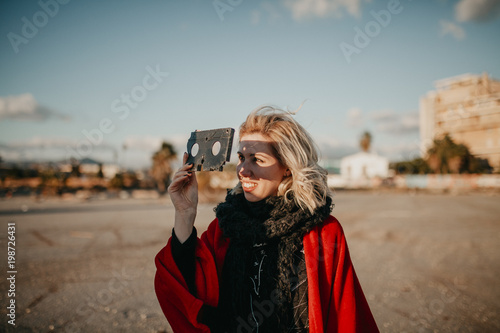 Fotografie, Obraz Blonde alternative woman playing with a VHS tape outdoors at sunset