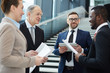 © pressmaster - Group of intercultural business partners or delegates in suits discussing their ideas for reports before conference