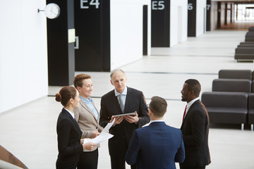 Canvas Print - Group of contemporary business people making circle while communicating in lounge of airport