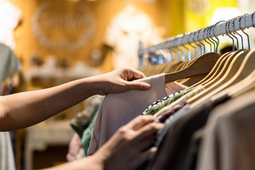 close up of woman hand choosing thrift young and discount t-shirt clothes in store, searching or buy
