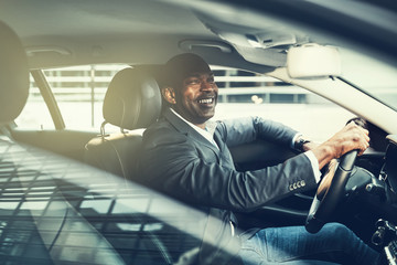 Canvas Print - Smiling African businessman driving through city traffic