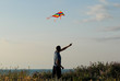 © ruslanshug - one active young man controls colorful kite floating in air at sunset near sea shore
