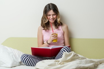 Wall Mural - Girl teenage high school student reading a textbook sitting at home in bed