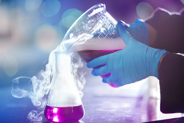 Wall Mural - hands of a scientist pouring pink liquid with white smoke from a laboratory glassware to another