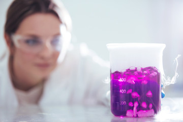 Wall Mural - young woman scientist working with laboratory glassware with pink liquid and white smoke in a labora