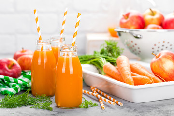 Wall Mural - Fresh carrot and apple juice on white background. Carrot and apple juice in glass bottles on white table. Apple and carrot juice on white background