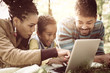 © Mladen - Cheerful African American family lying down in park and  using laptop.