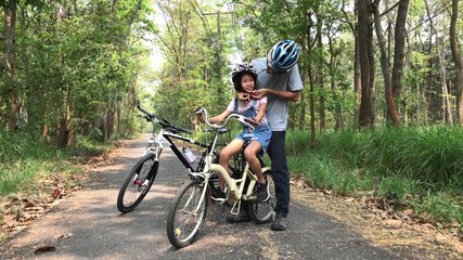 Wall Mural - Happy father and daughter cycling in the park wears a bicycle helmet to his daughter, togetherness relaxation concept