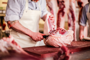 butcher cut raw meat of a pig with a knife at table in the slaughterhouse